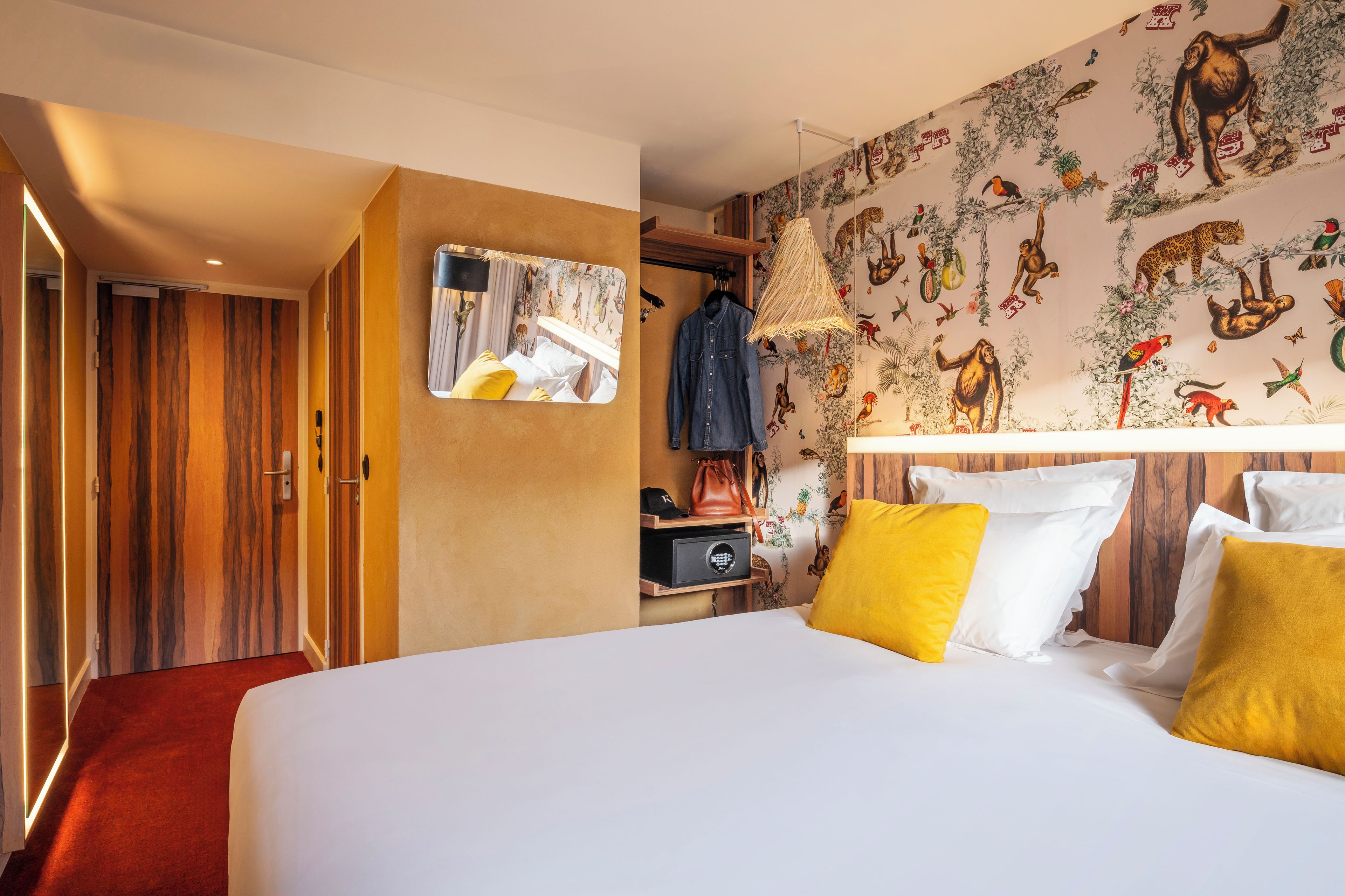A hotel room with a large bed, a wardrobe, a mirror, and a wall with animal illustrations.