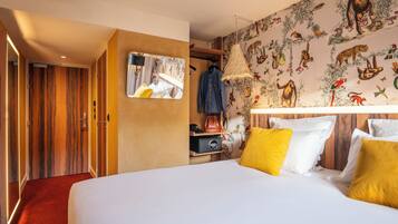 A hotel room with a large bed, a wardrobe, a mirror, and a wall with animal illustrations.