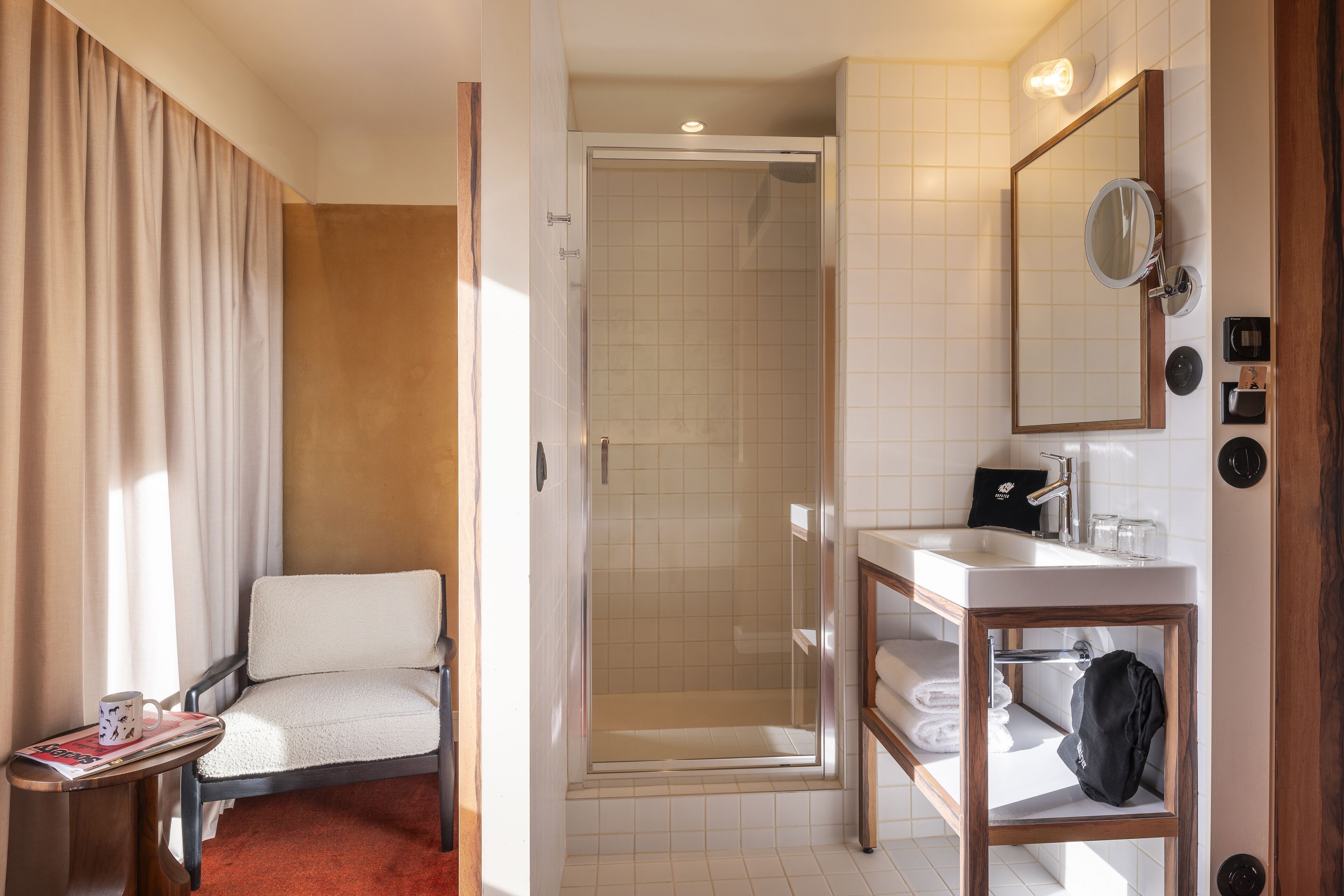 A hotel bathroom with a shower, a sink, a mirror, and a chair.