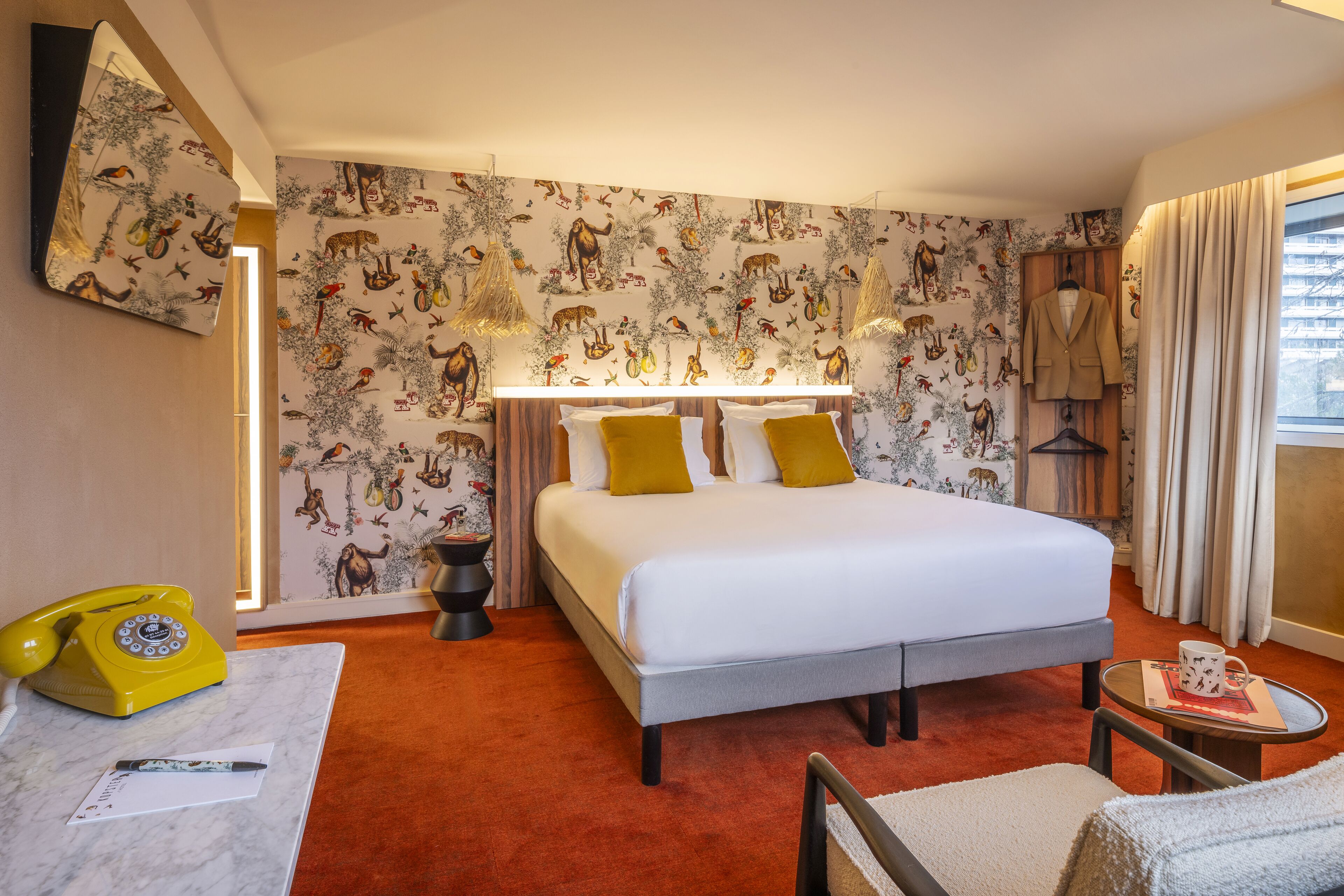 A hotel room with a bed, a desk with a telephone, a chair, and a window with curtains.