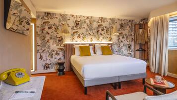 A hotel room with a bed, a desk with a telephone, a chair, and a window with curtains.