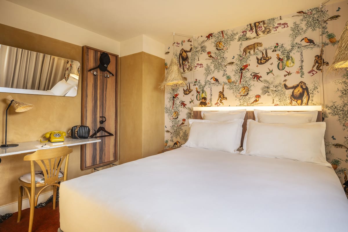 Hotelkamer met een bed, een bureau met stoel, een spiegel en een muur met een natuurdecoratie.