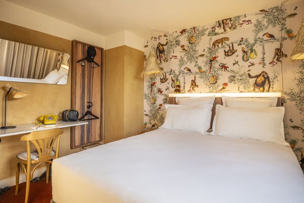 Habitación de hotel con cama, escritorio con silla, espejo y un mural temático de naturaleza en la pared.