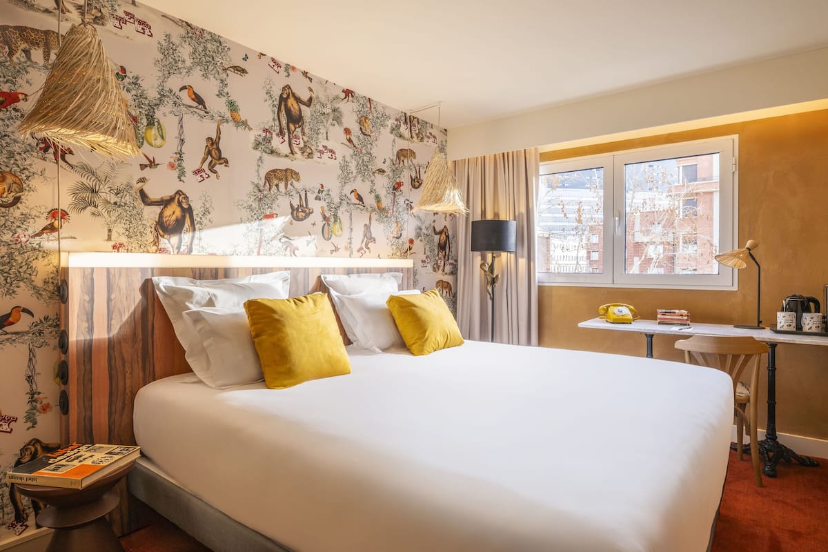 Een hotelkamer met een groot bed, een bureau met lamp en een raam met gordijnen.