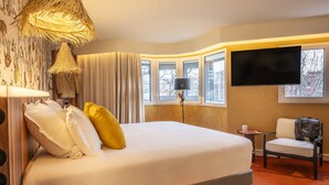 Une chambre d’hôtel avec un grand lit, une télévision, une chaise et une fenêtre donnant sur des immeubles.