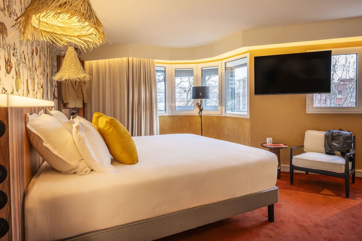 Een hotelkamer met een groot bed, een televisie, een stoel en een raam met uitzicht op gebouwen.