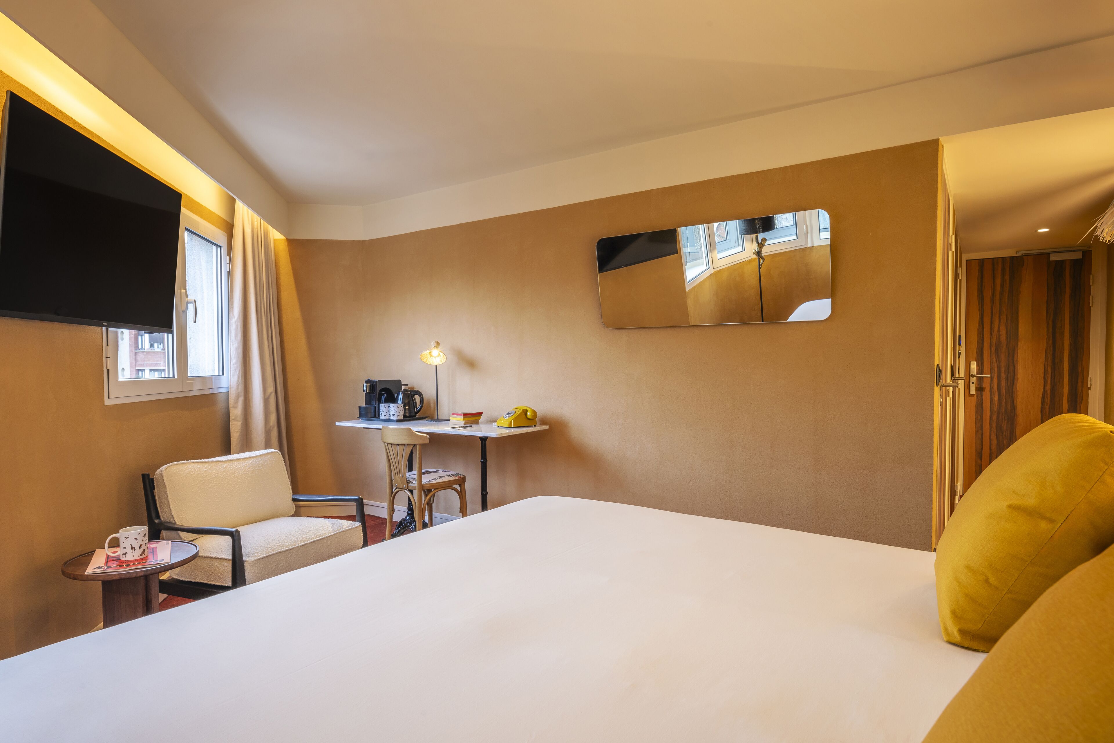 A hotel room with a bed, a desk, a chair, a TV, and a mirror.