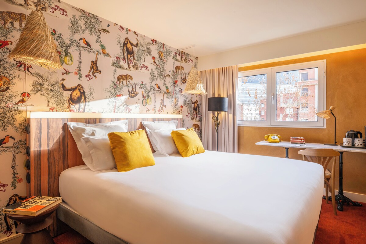 Une chambre d’hôtel avec un grand lit, un bureau avec une lampe et une fenêtre avec des rideaux.