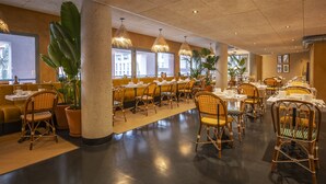 Un restaurant spacieux avec de hauts plafonds, des chaises en osier et des plantes en pot.
