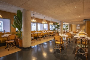 Un restaurante espacioso con techos altos, sillas de mimbre y plantas en macetas.