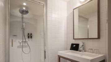 Une salle de bain moderne avec une douche à parois de verre, un lavabo blanc avec un miroir au-dessus, et deux petites bouteilles fixées au mur.