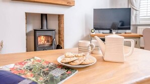 Ein gemütliches Wohnzimmer mit Kamin, Fernseher und einem Tisch mit Keksen und einer Tasse.