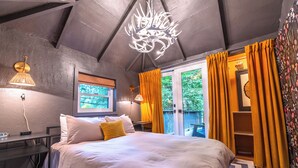 A bedroom with a bed, a chandelier, a window with curtains, and a view of greenery outside.