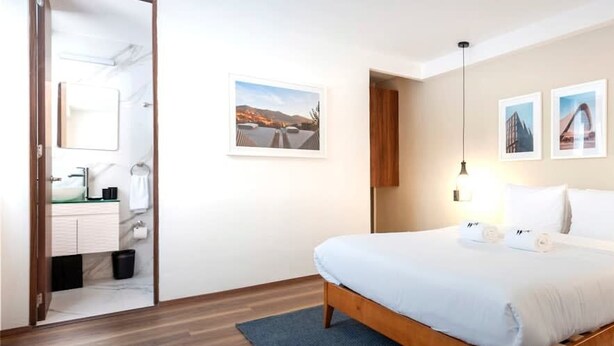 A hotel room with a bed, bedside tables, a nightstand, a wooden floor, and a bathroom visible through an open door. - w* | Cool 1BR with Amazing Deco in Polanco (Ciudad de México)