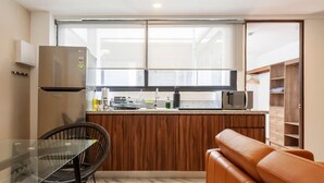 A compact kitchen with a built-in oven, a dining area with a glass table and a black chair, and a wooden cabinet with a hanging rack. - w* | Cool 1BR with Amazing Deco in Polanco (Ciudad de México)