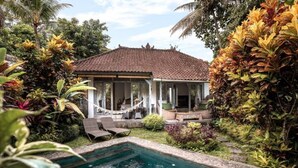 Ein Haus mit Ziegeldach, umgeben von üppiger tropischer Vegetation und einem Schwimmbad.