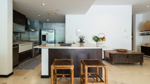 A modern kitchen with a central island, two stools, a coffee machine, and a fruit basket. - NEW LISTING! PRIVATE POOL CONDO ON 5TH AVE, BBQ, PARKING, 2min walk to beach (Playa del Carmen)