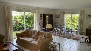 A living room with a beige sofa, a glass coffee table, and a dining area with metal chairs and a chandelier. - House with private pool near the sea (Lanton)
