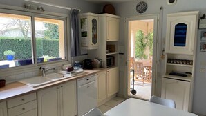A compact kitchen with white cabinetry, a sink, a microwave, and a dining area with a table and chairs. - House with private pool near the sea (Lanton)