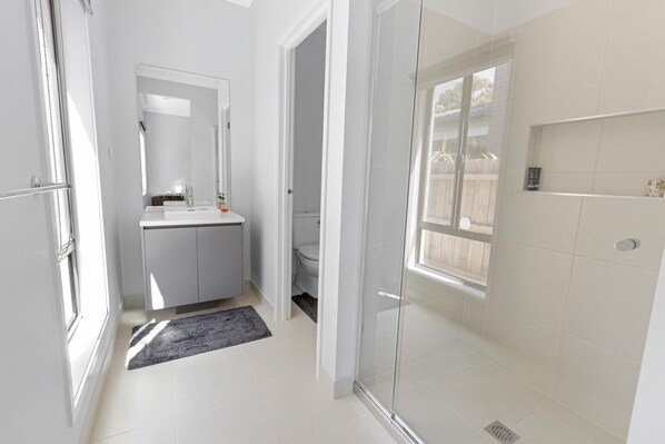 Un baño moderno con mampara de vidrio, un lavabo blanco y un espejo encima.