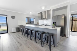Cocina moderna con una isla central, taburetes de bar, un refrigerador de acero inoxidable y vistas al exterior.