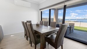 Uma sala de jantar com uma mesa grande e cadeiras, vista para o mar através de amplas janelas e decoração interior moderna.