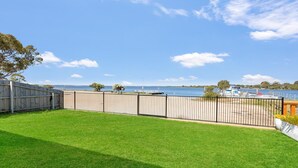 Quintal cercado com gramado, cerca de madeira e vista para um lago com barcos.
