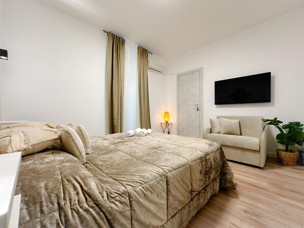 Un dormitorio con cama, sofá, televisor y una planta en maceta.