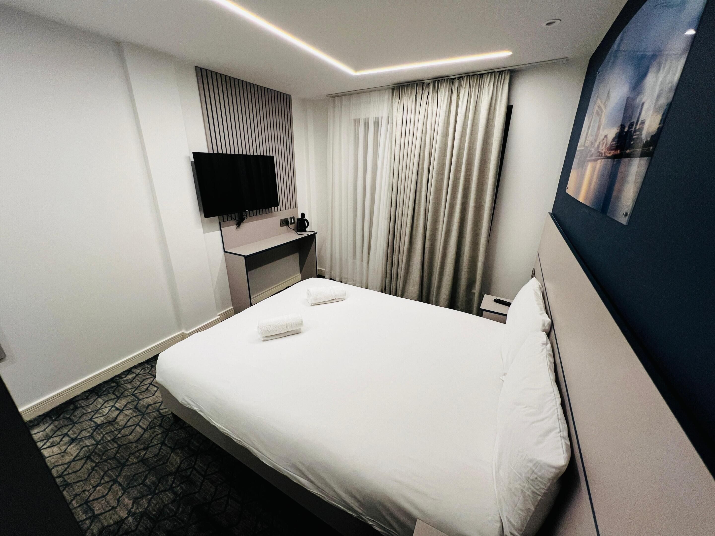 Une chambre d’hôtel avec un lit, un bureau, un téléviseur à écran plat, un tableau et une fenêtre avec des rideaux.