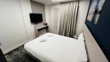 A hotel room with a bed, a desk, a flat-screen TV, a painting, and a window with curtains.