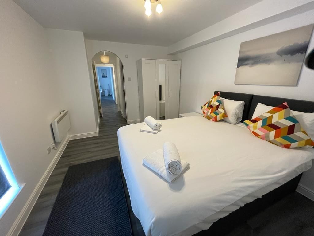 Habitación de hotel con una cama grande, un armario, un cuadro en la pared y un pasillo que conduce a otra habitación.