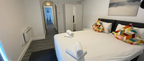 Habitación de hotel con una cama grande, un armario, un cuadro en la pared y un pasillo que conduce a otra habitación.