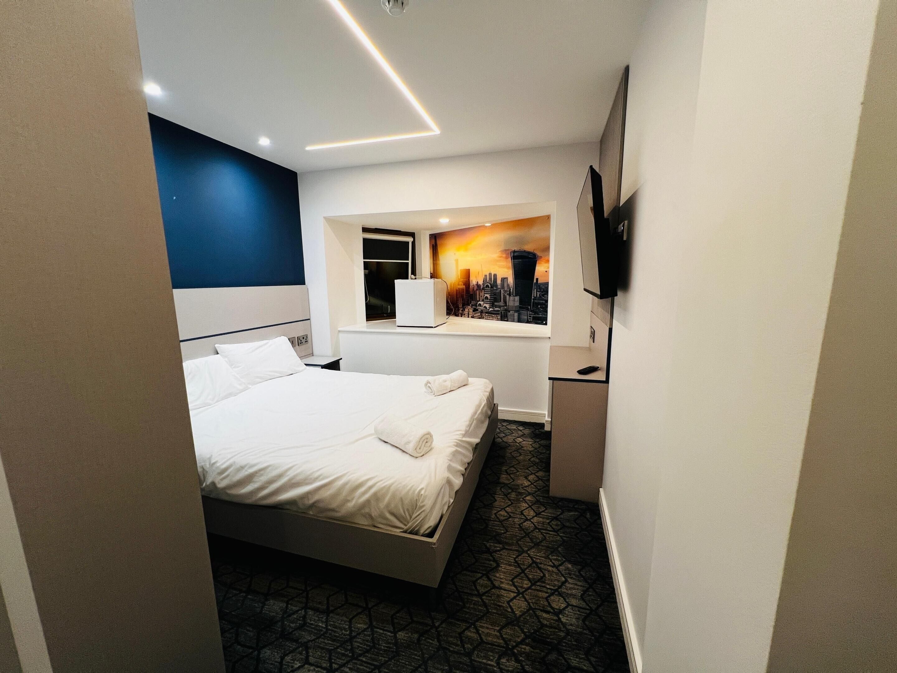 A hotel room with a bed, a cityscape mural, a television, and a window.