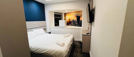 A hotel room with a bed, a cityscape mural, a television, and a window.