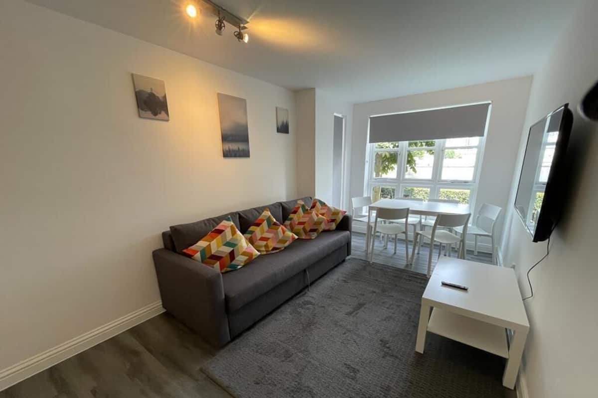 A modern living room with a grey sofa, a white table, and a TV mounted on the wall.