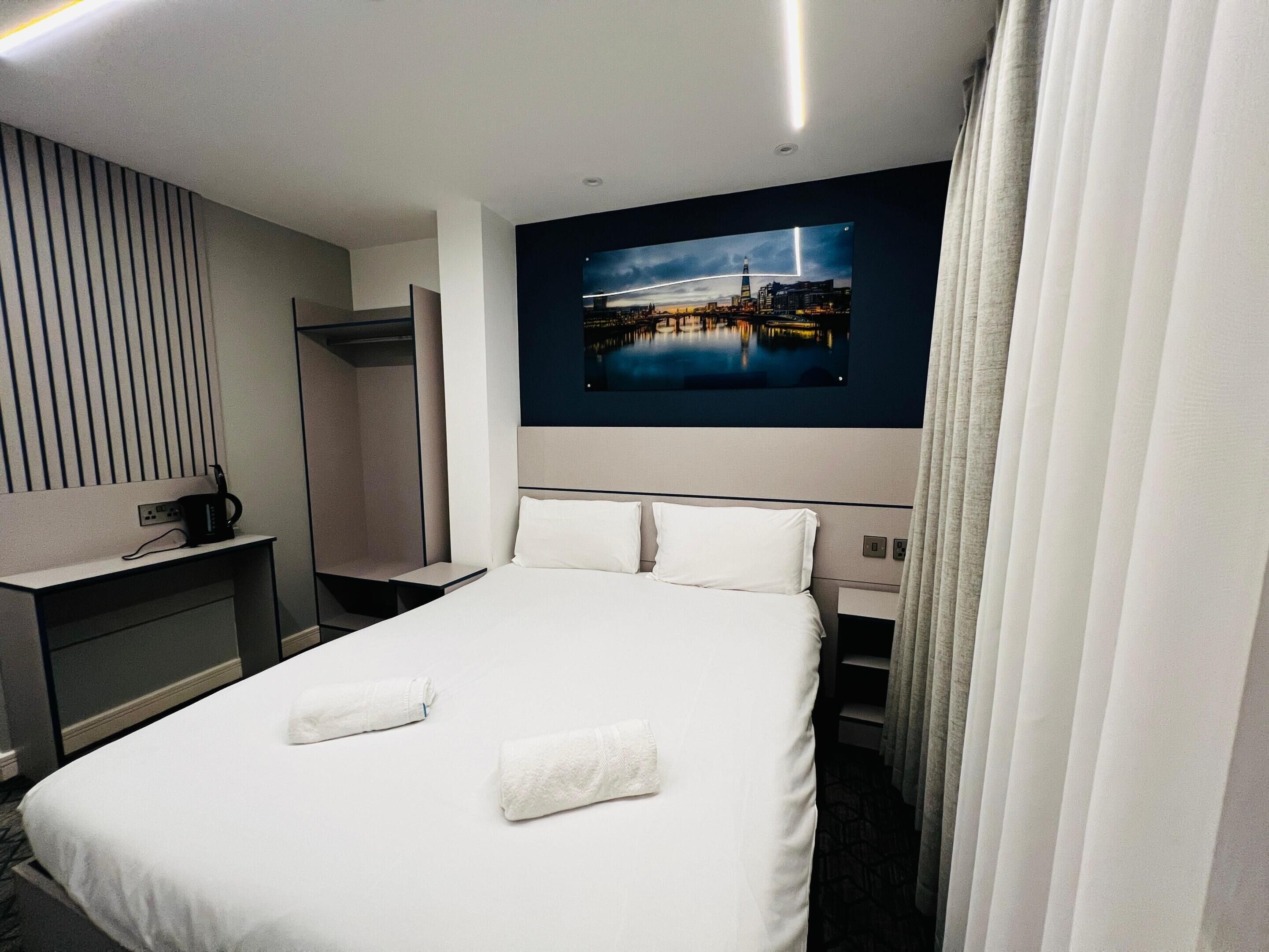 A hotel room with a large bed, a desk with a computer, a mirror, and a view of a cityscape.
