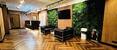A modern reception area with a wooden floor, a reception desk, black leather seating, a wall-mounted TV, and a green vertical garden.
