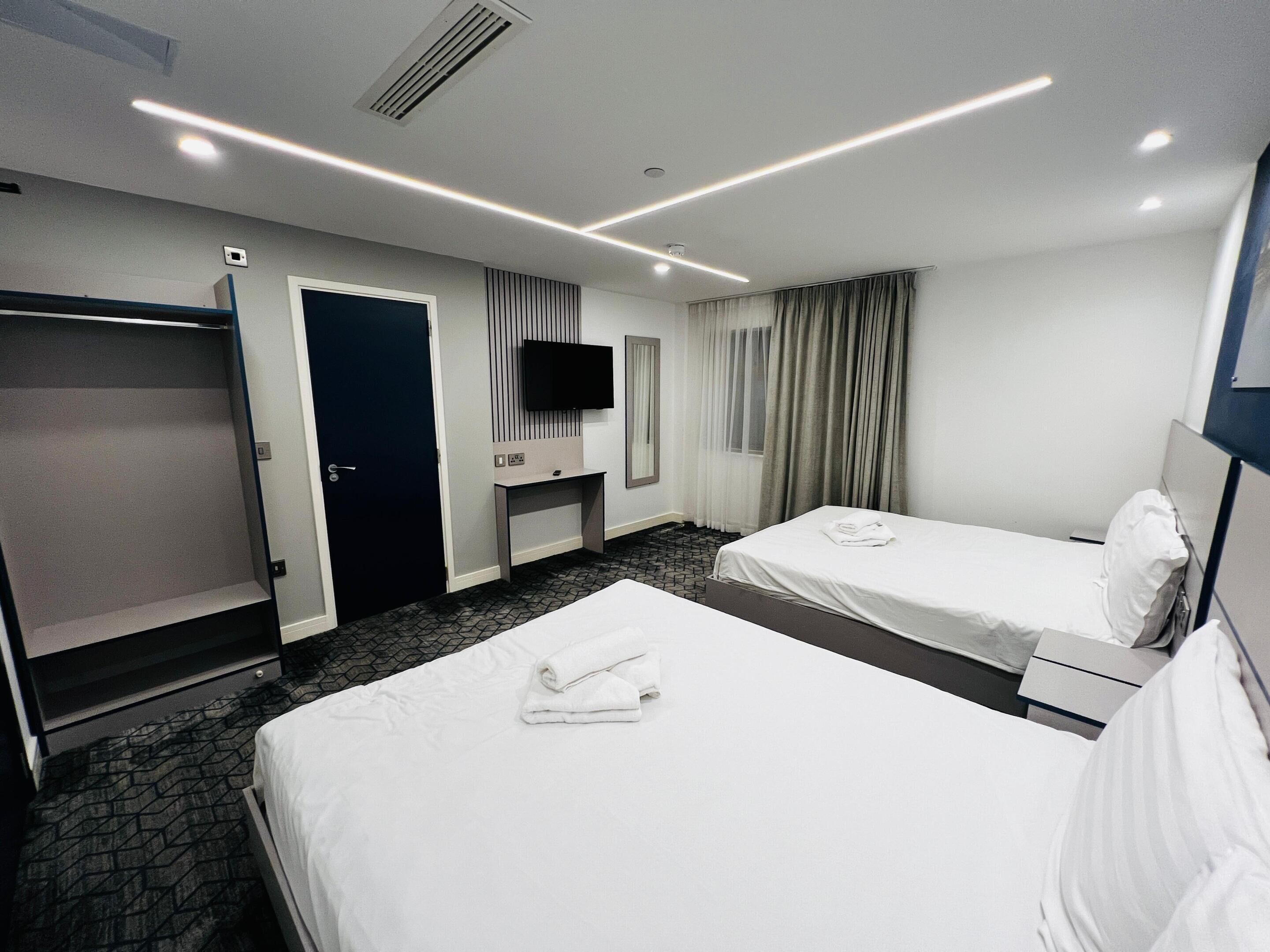 Habitación de hotel con dos camas, televisión, escritorio y armario.