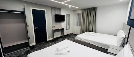 Quarto de hotel com duas camas, televisão, escrivaninha e guarda-roupa.