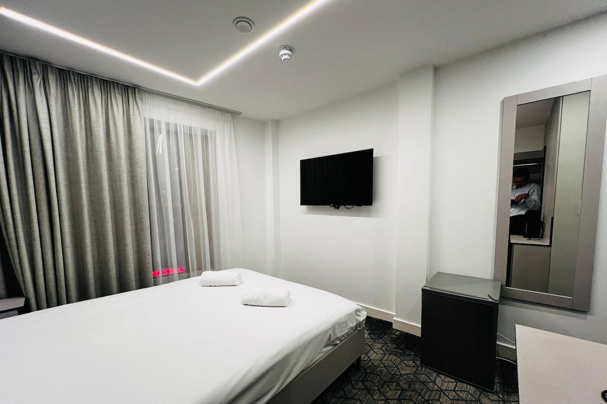 A hotel room with a bed, a TV mounted on the wall, a mirror, and a small desk.