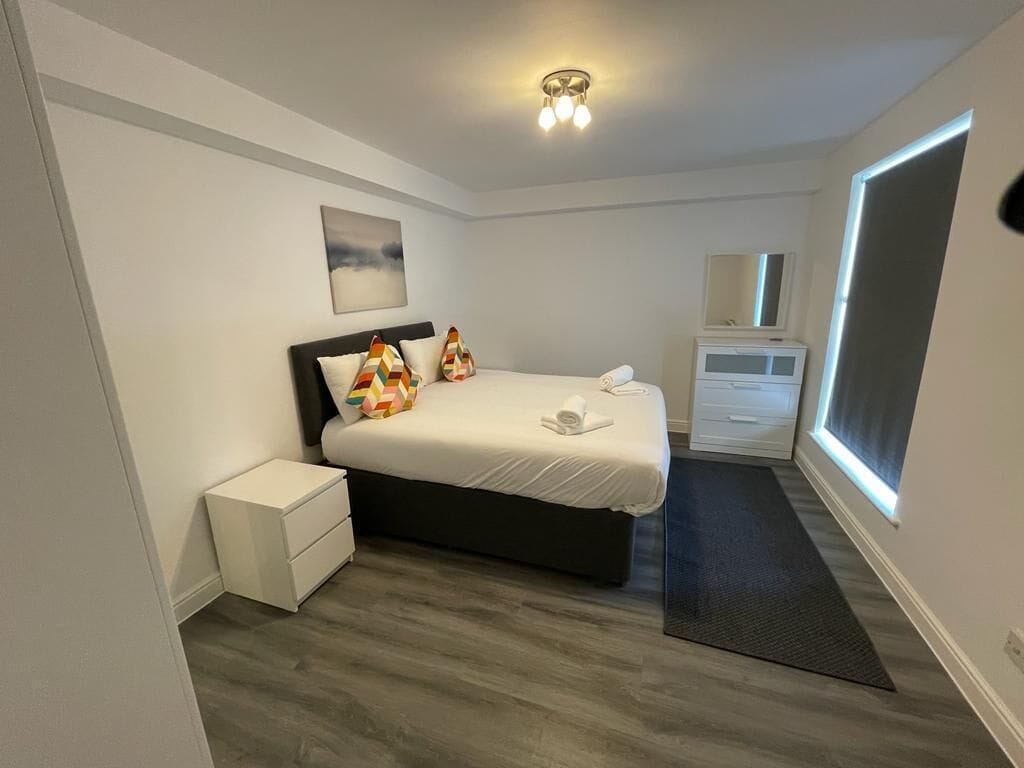 A bedroom with a bed, bedside table, dresser, and a window.
