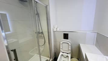 A modern bathroom with a glass-enclosed shower, a toilet, and a trash bin.