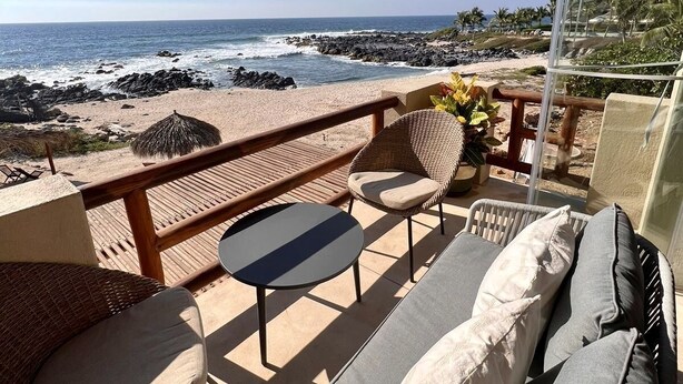 A balcony with wicker furniture, a glass door, and a view of the ocean.