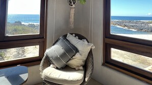 A corner room with a wicker chair, a small table, and a view of the ocean through large windows.