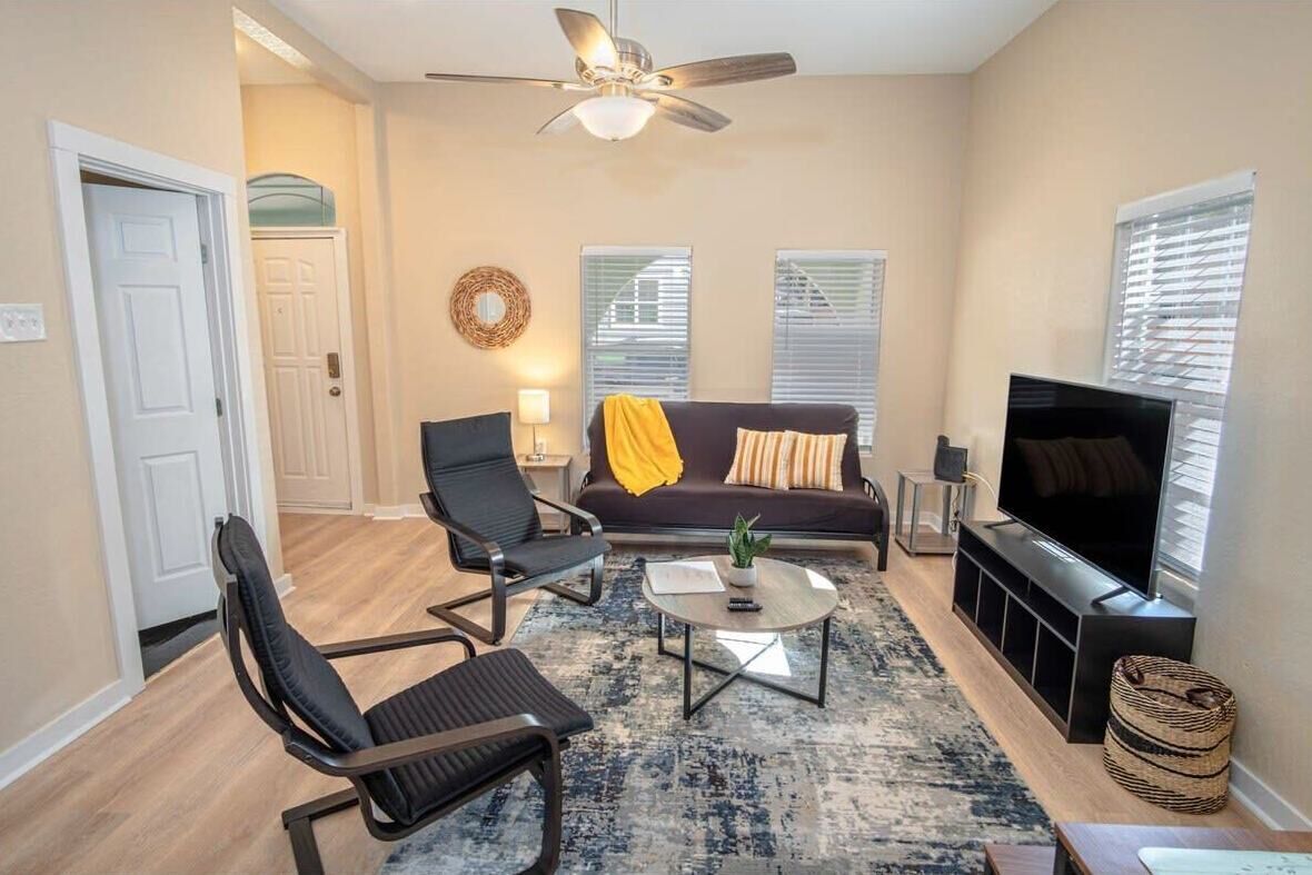 A living room with a sofa, two chairs, a coffee table, a TV, and a ceiling fan.