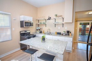 A kitchen with a central island, white cabinets, stainless steel appliances, and a window with blinds.