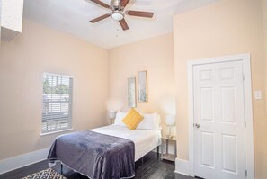 A bedroom with a bed, a ceiling fan, a window with blinds, and a door.