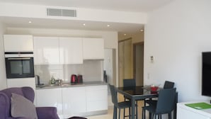 Eine moderne Küche mit weißen Schränken, einem Esstisch mit vier Stühlen und einem violetten Sofa.