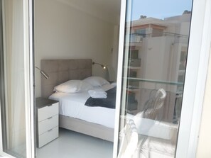 Un dormitorio con cama, mesita de noche, lámpara y vistas al exterior a través de un ventanal.