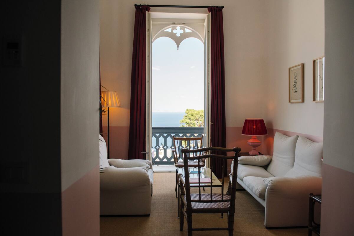 A room with a balcony, a sofa, a chair, and a lamp.